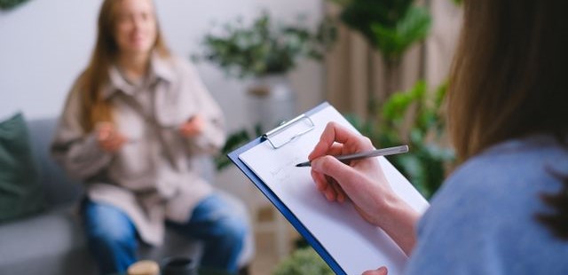 A clinical practitioner taking detailed intake notes on a clipboard during a patient's customized wellness strategy consultation