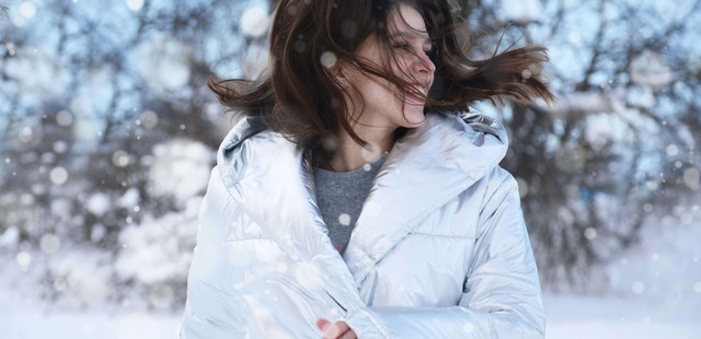 A smiling, vibrant woman in a silver winter coat enjoying the outdoors to represent emotional resilience and stress downregulation benefits