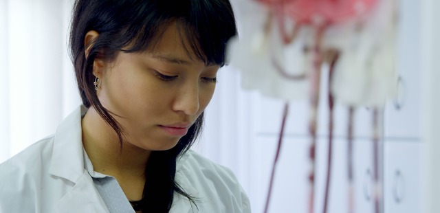 female-scientist-conducting-blood-research-in-laboratory A female clinical researcher in a white lab coat meticulously examining medical data or laboratory equipment, symbolizing the evidence-based research behind wet cupping therapy.