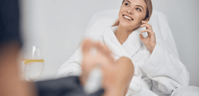A smiling female patient in a white robe receiving clinical foot reflexology to stimulate systemic relaxation and vascular circulation