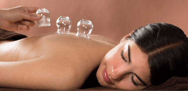 practitioner-doing-a-dry-cupping-on-a-females-back-while-she-is-lying-flat Practitioner applying transparent glass vacuum cups to a patient's back to perform clinical dry cupping therapy for myofascial decompression