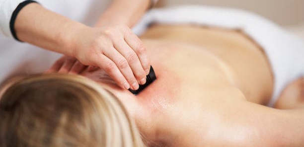 Clinical practitioner applying press-stroke friction using a black horn scraping tool to perform clinical Gua Sha therapy on a patient's upper back