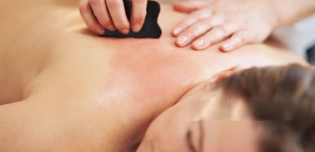 Practitioner applying press-stroke friction using a smooth black scraping tool to induce therapeutic petechiae during clinical Gua Sha therapy